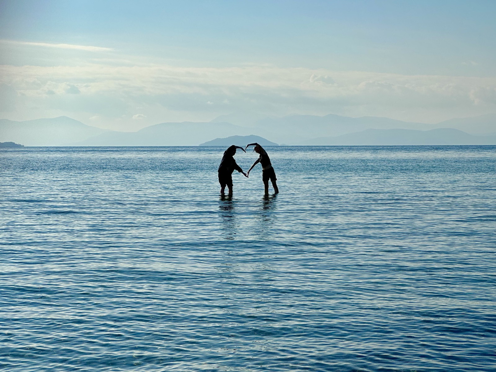 Two travelers forming a heart with their arms in the calm sea
