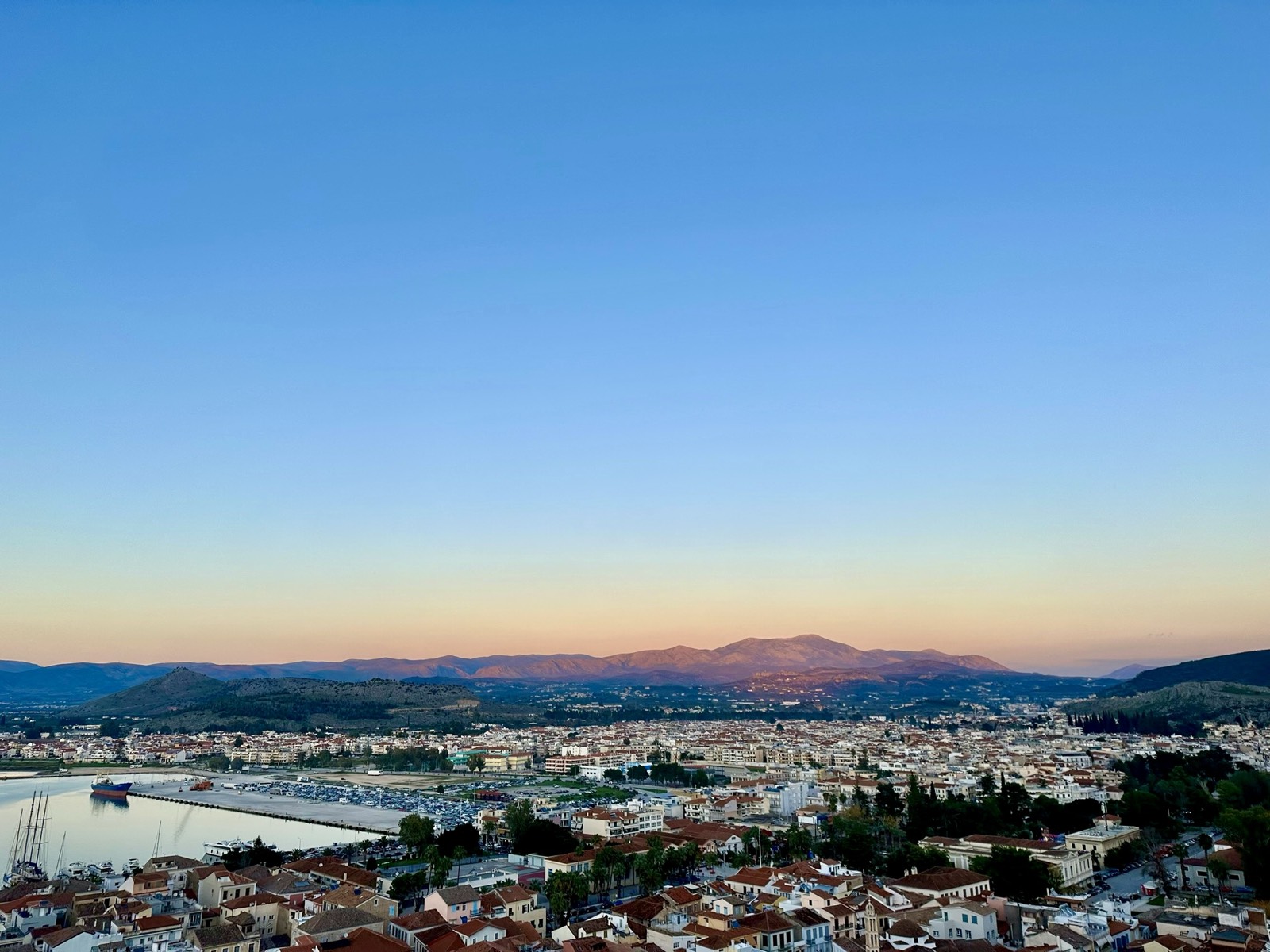 A hilltop panorama over a Greek coastal town at dusk
