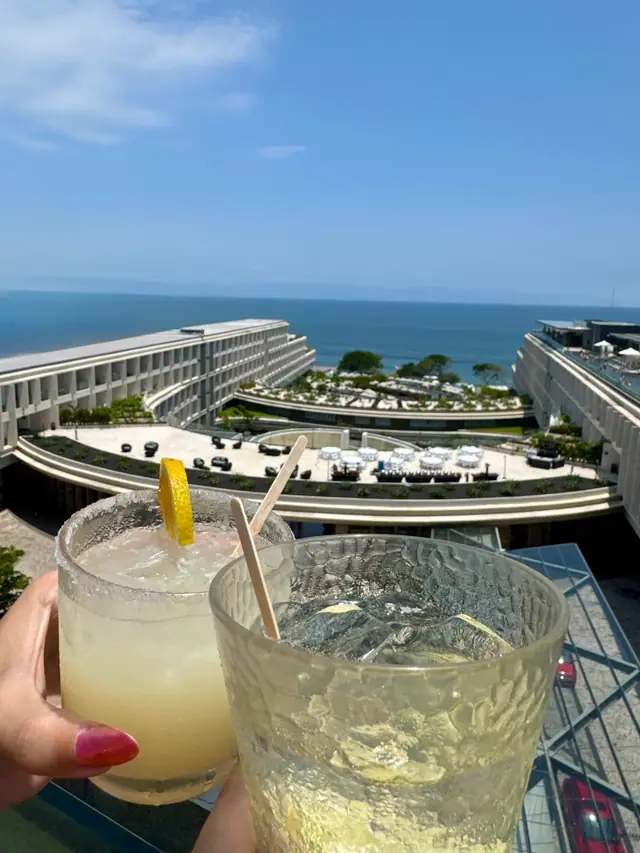Two cocktails raised over a rooftop view of the ocean