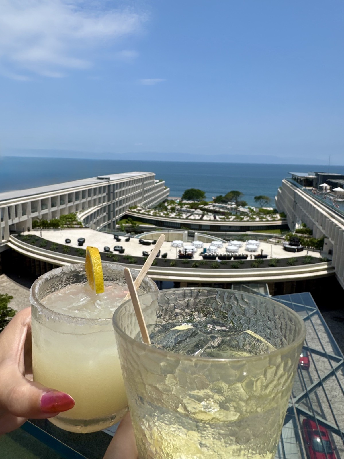 Two cocktails raised over a rooftop view of the ocean