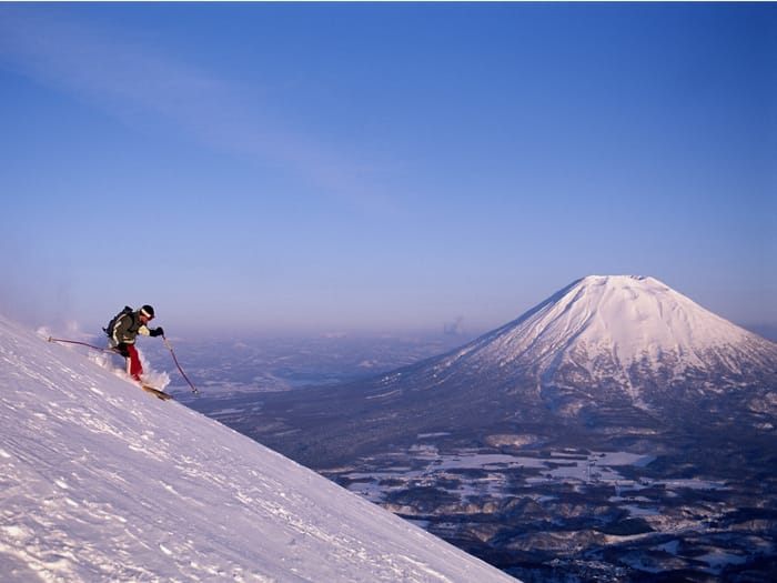  A Skier cruising down a mountain in Niseko with Mount Yotei in the background