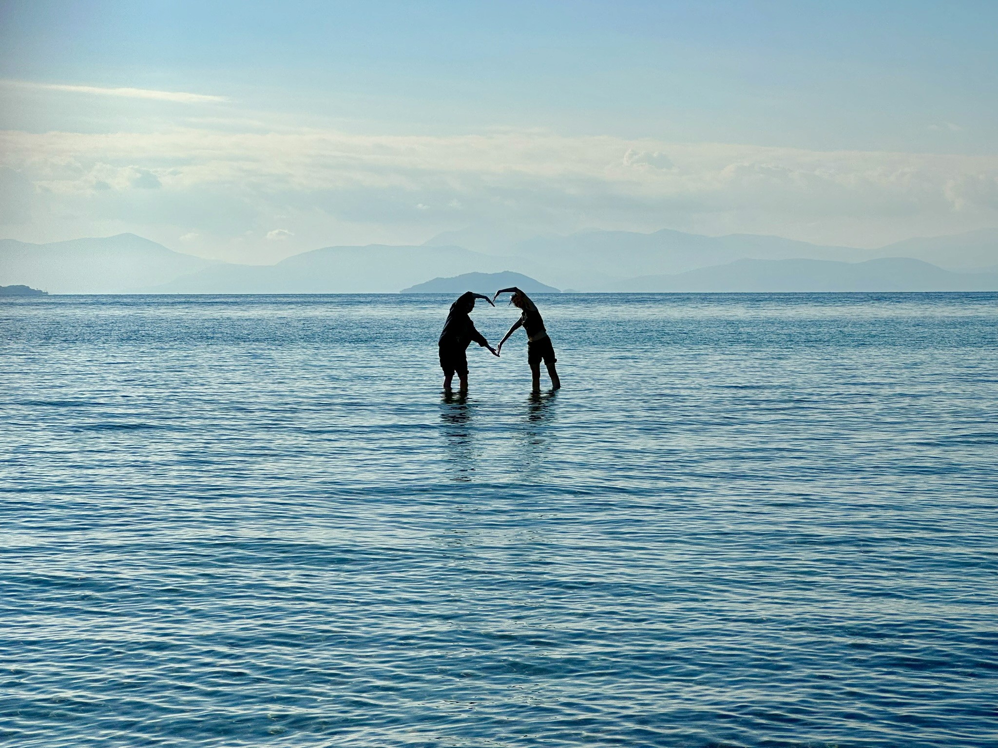 Two people standing in the Mediterranean Sea forming a heart shape with their arms.